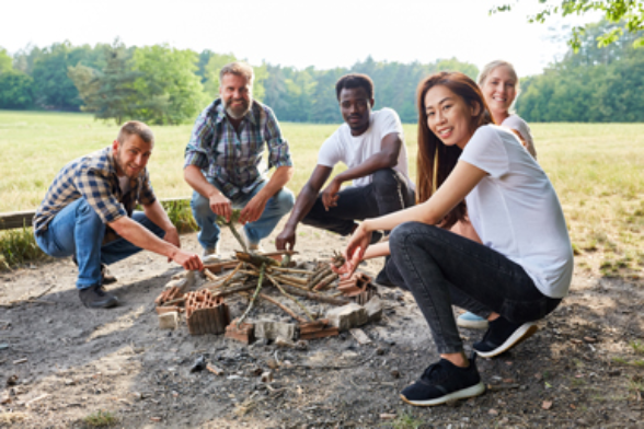 Mehrere Personen sitzen um ein Lagerfeuer.