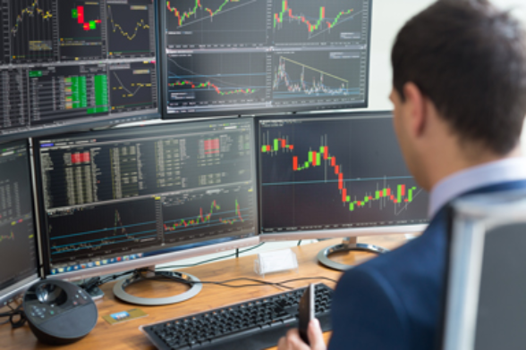 Ein Mann analysiert mehrere Bildschirme mit Börsenkursen.