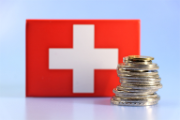 Schweizerflagge als Hintergrund, davor ein Turm aus Münzen.