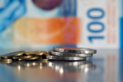 Münzen im Wert von fünf Franken und fünf Rappen vor einem 100-Franken-Schein.