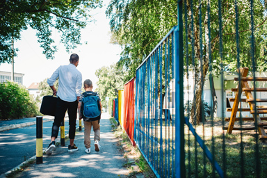 Ein Mann begleitet ein Kind auf dem Weg zur Schule.