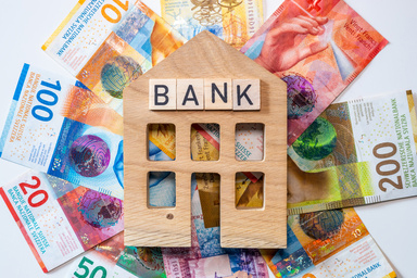 Banknoten unter einem Holzhäuschen mit der Aufschrift "BANK"