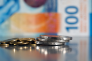 Five franc and five cent coins in front of a hundred dollar bill.