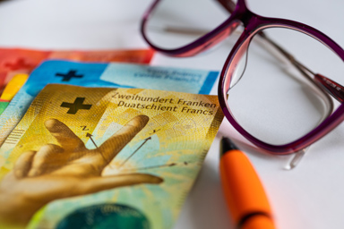 Swiss banknotes, a pair of glasses, and a pen