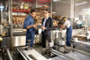 A woman in formal attire converses with an employee in a factory.