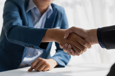 Two people shake hands across a desk.