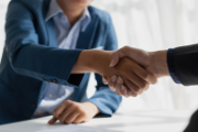 Two people shake hands across a desk.