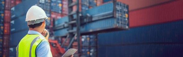 A man wearing an helmet and a safety vest inspects the unloading of a container.