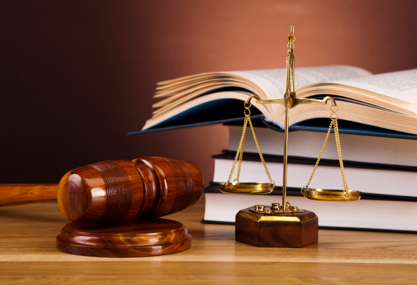 A hammer and a scale are placed in front of a pile of law books.