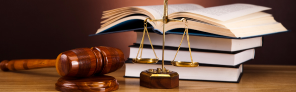 A hammer and a scale are placed in front of a pile of law books.