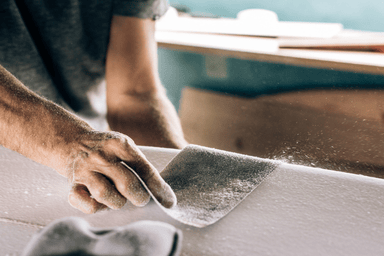 A person sands down a surfboard