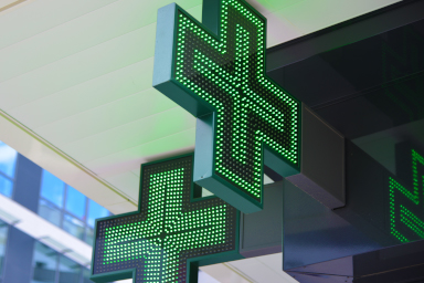 Une croix verte est accrochée au-dessus de l’entrée d’une pharmacie.