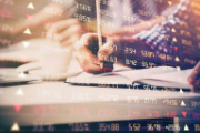 Une personne écrit dans un cahier. En surimpression figure un tableau des cours de la bourse.