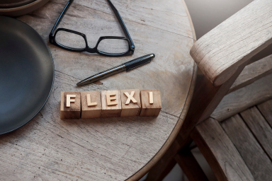 Des lunettes et un stylo posés sur une table avec le terme "flexi" en dés de bois