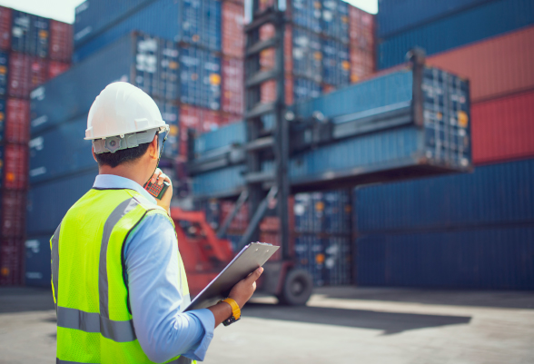 Un homme muni d'un casque et d'un gilet de sécurité inspecte le déchargement d'un container.