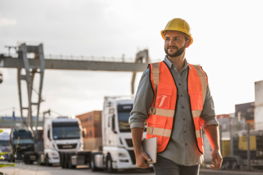 Un uomo che indossa un casco e un gilet di sicurezza davanti ad alcuni camion