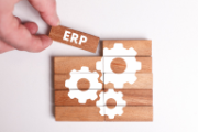 Una persona aggiunge un ultimo pezzo ad un puzzle in legno, sul quale figurano degli ingranaggi e la sigla ERP, sinonimo di software di gestione integrata.