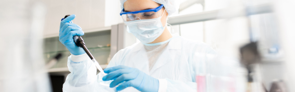 Une donna dotata di materiale di protezione usa una pipetta in un laboratorio.